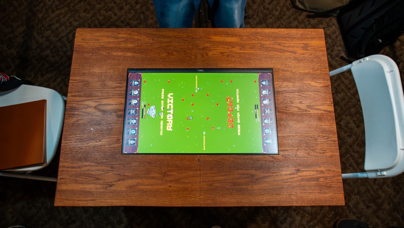 Top-down view of the UVULITES table mid-match — the embedded screen surrounded by the wooden play surface